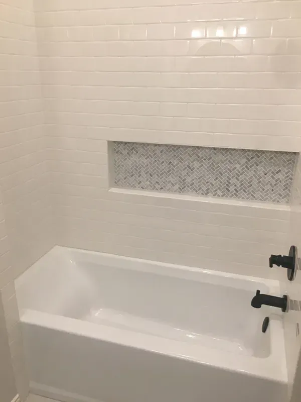 White bathtub with subway tile walls and a mosaic tile niche. Black faucet.
