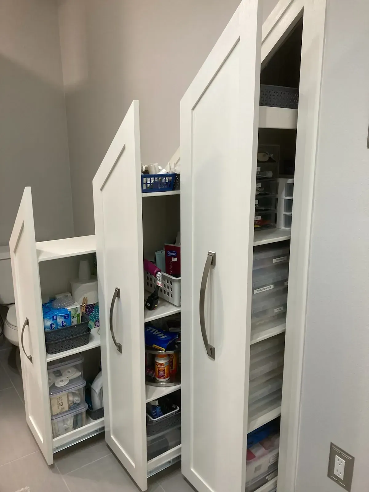 White storage cabinets with open doors in a bathroom. Various items stored inside.