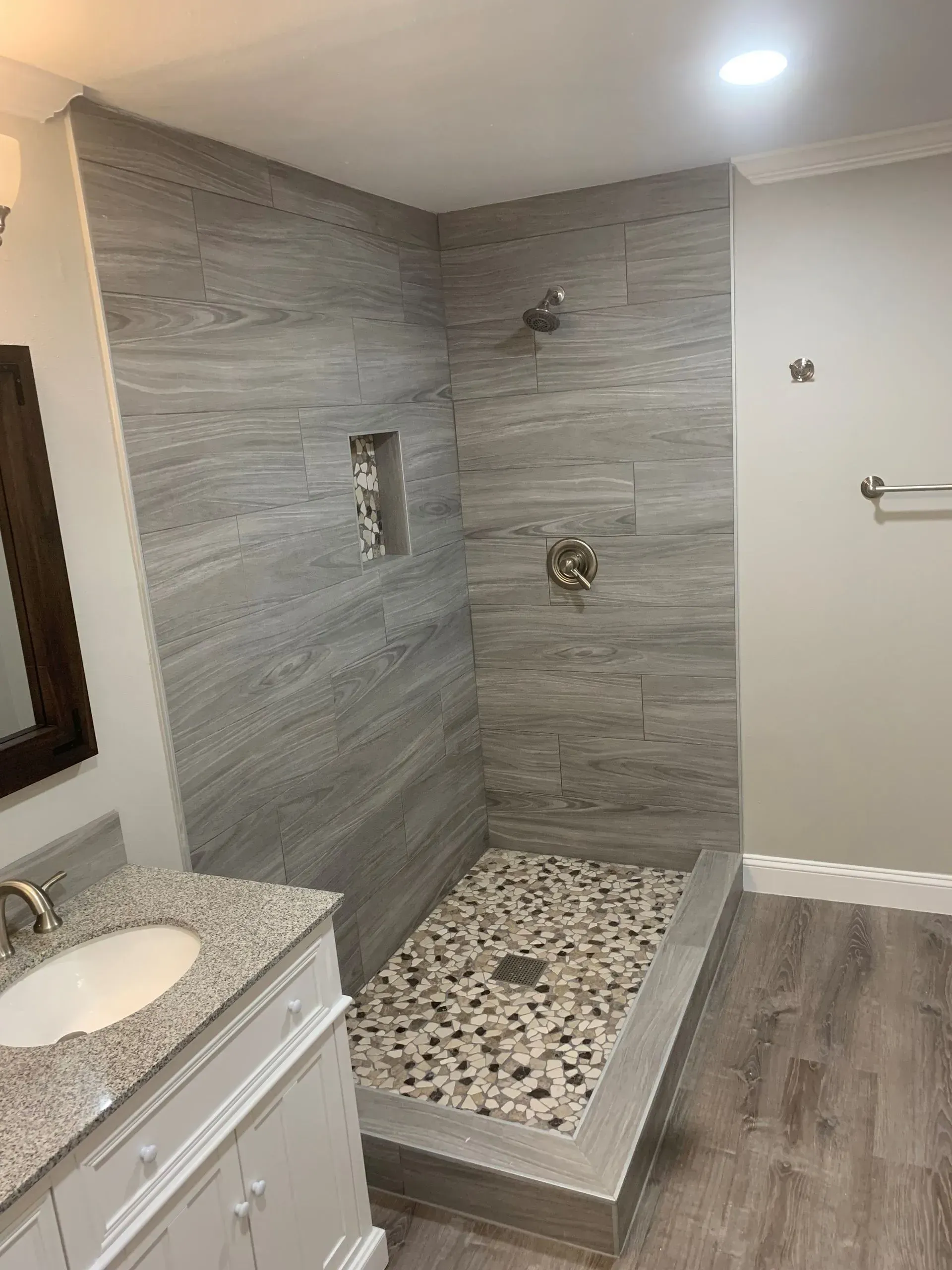 Bathroom with gray tiled shower and pebble floor, vanity with granite countertop.