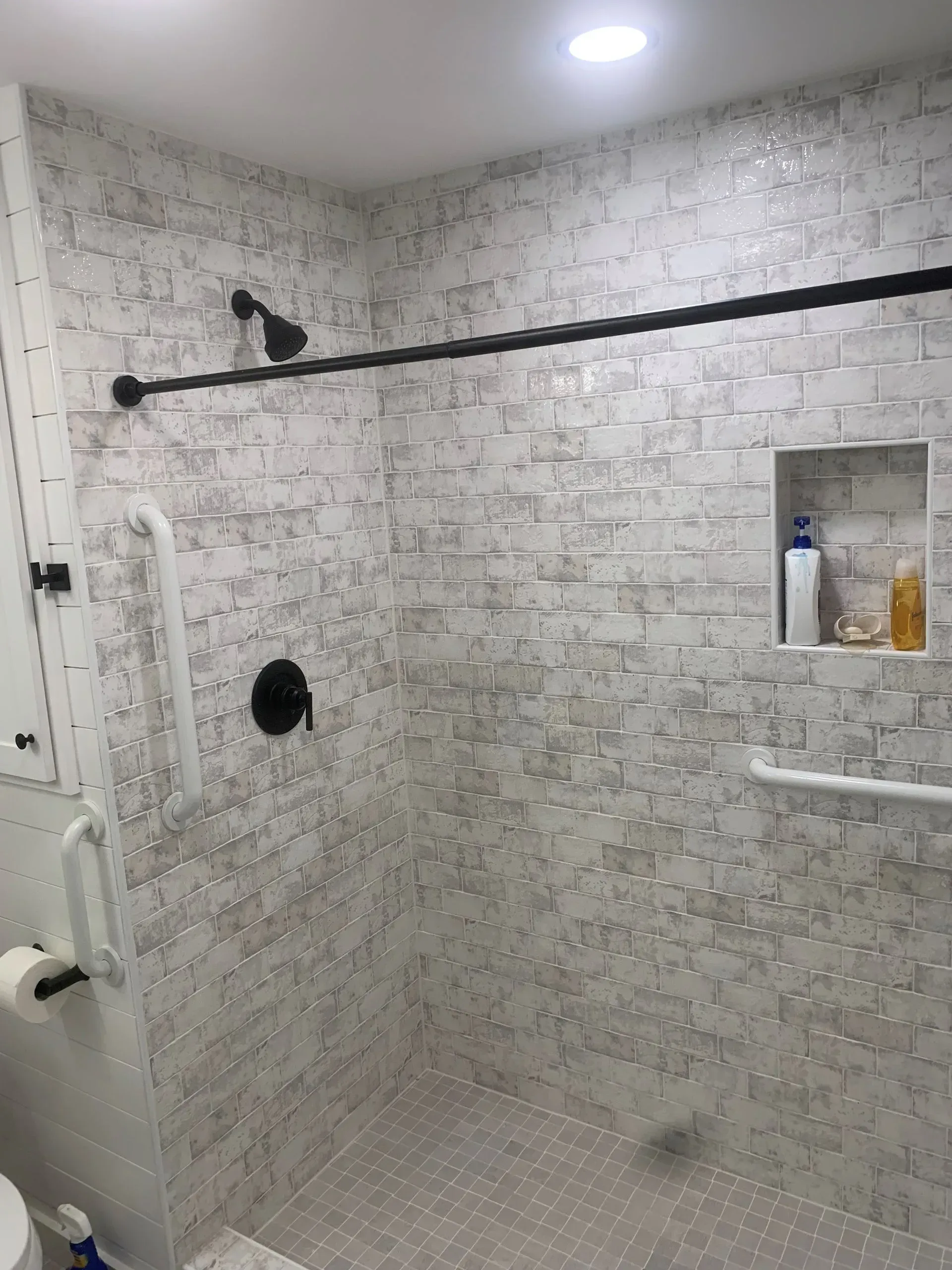 Accessible shower with gray tile, black fixtures, and grab bars.
