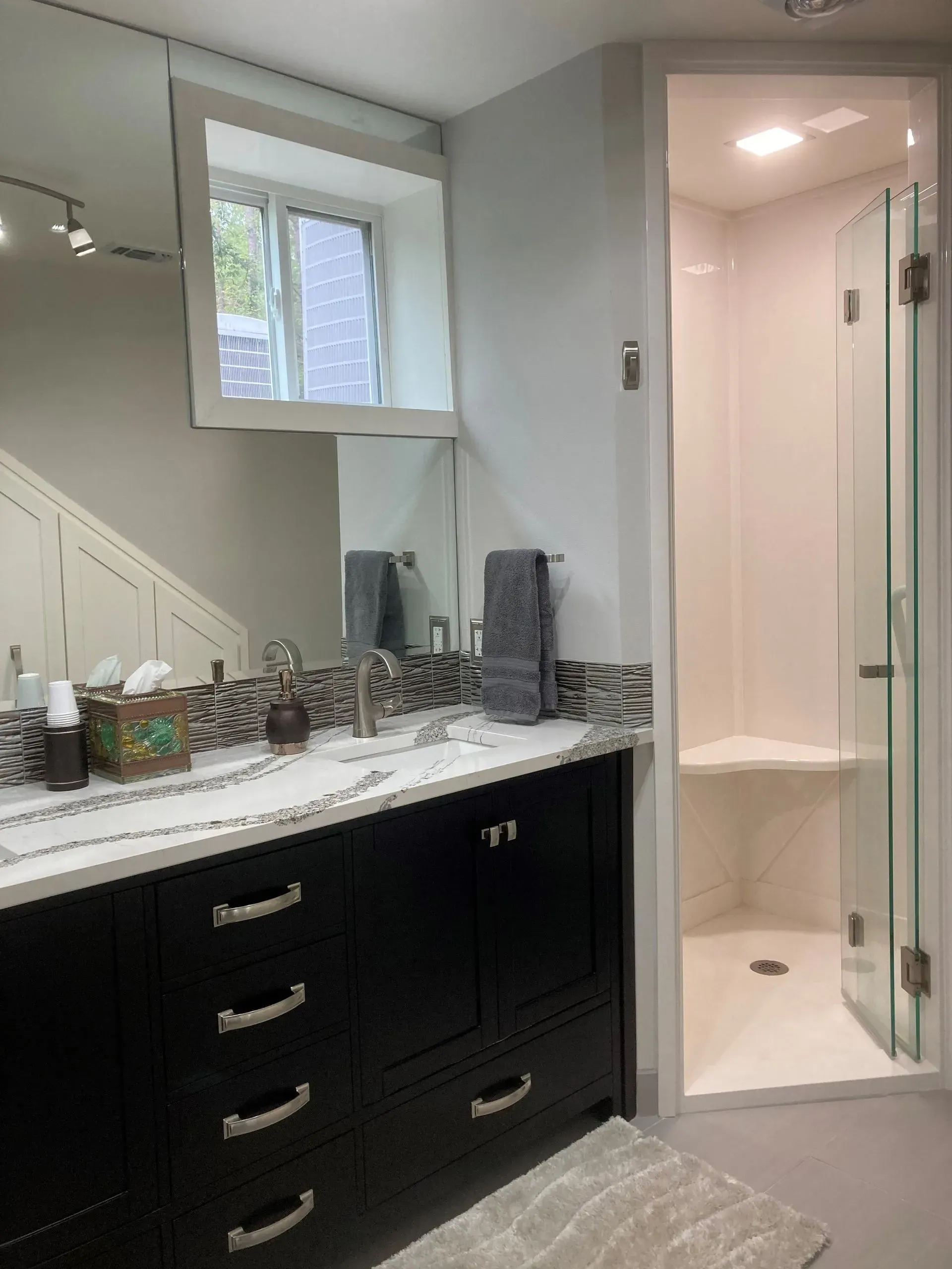 Bathroom with black vanity, white countertop, and glass shower.