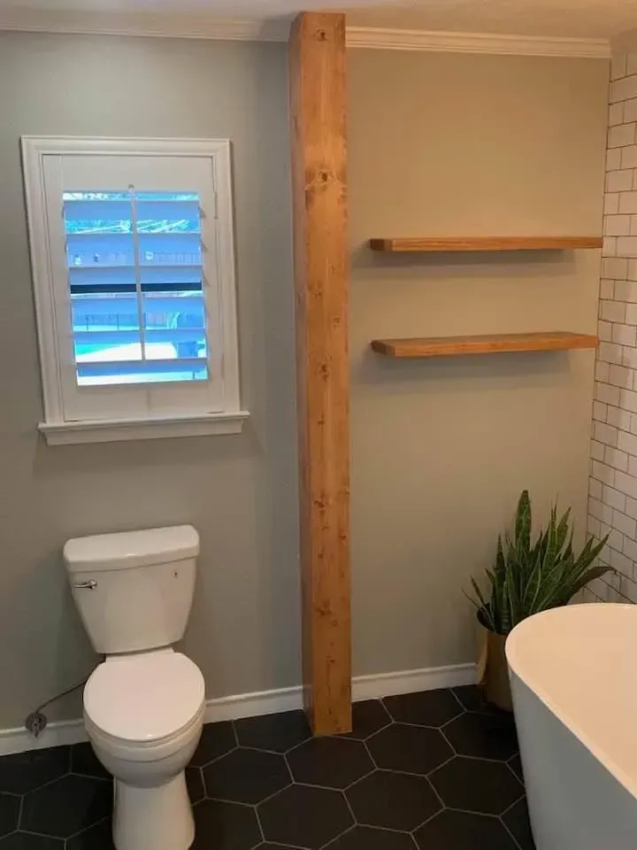Bathroom with toilet, wooden beam, shelves, window with shutters, and black tiled floor.