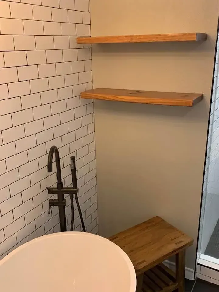 Bathroom with white subway tile, wood shelves, black faucet, tub, and wooden bench.