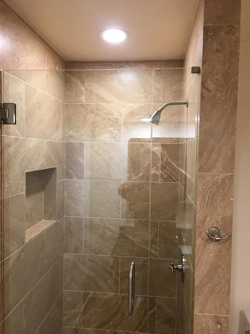 Shower with beige tiled walls, a glass door, and chrome fixtures.