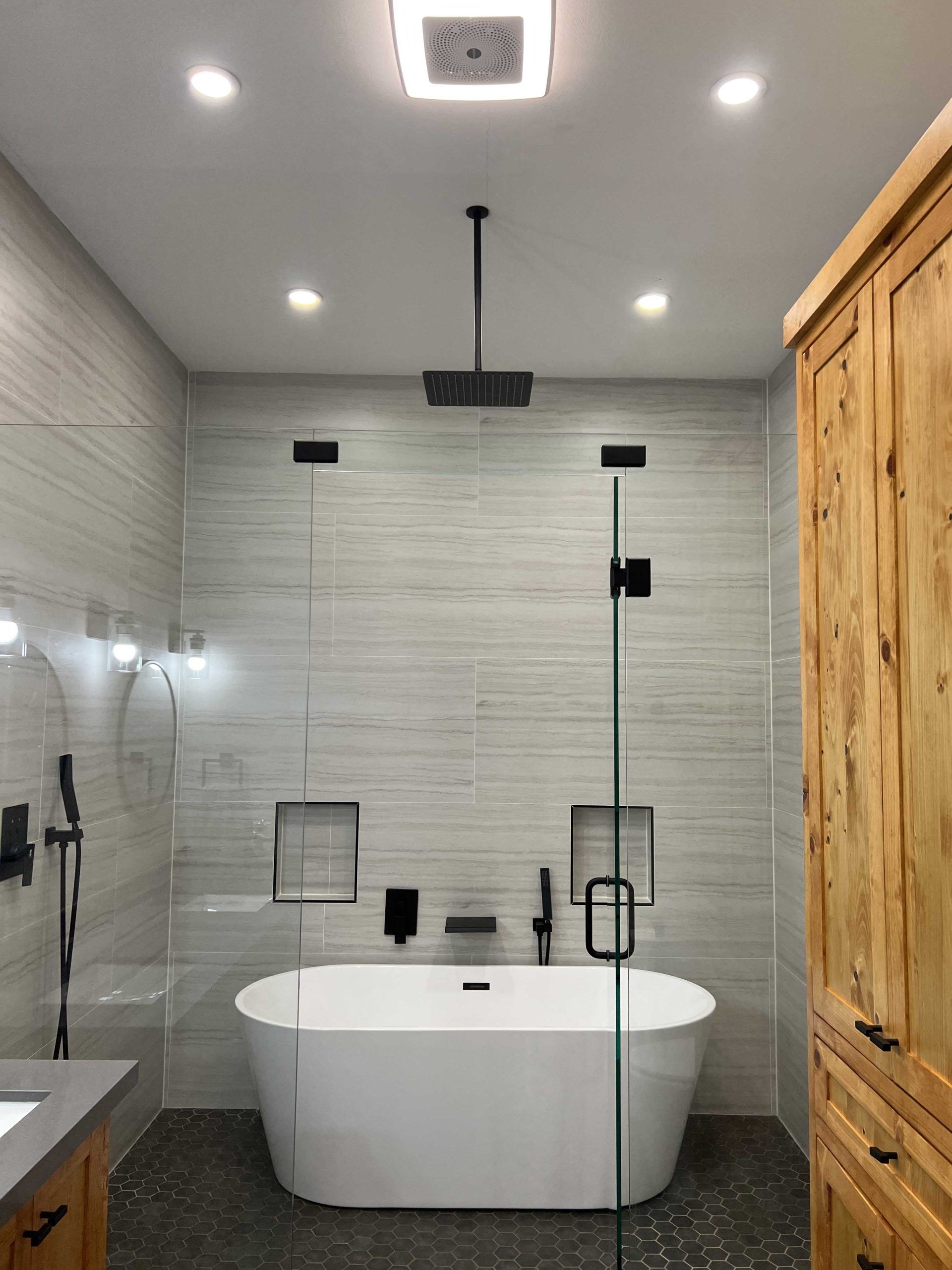 Modern bathroom with a white tub, glass shower, and light gray tiled walls.