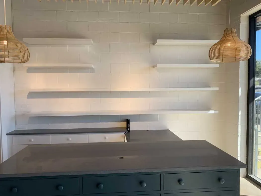 Kitchen with white shelves, navy island, grey countertops, and wicker pendant lights.