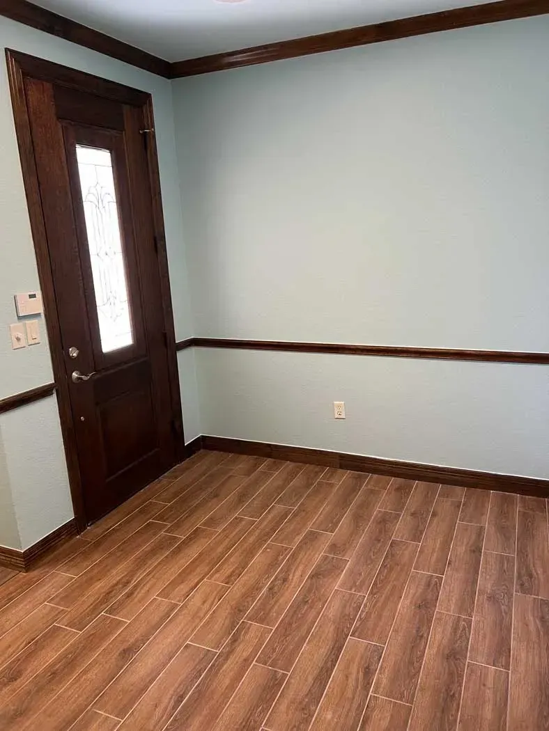 Empty room with wooden door, trim, and floor; walls are painted light blue.