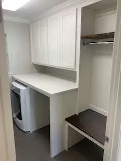 White laundry room with washer, countertop, cabinets, hanging rod, and dark bench.