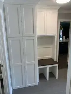 White built-in storage unit with cabinets and a bench in a hallway.