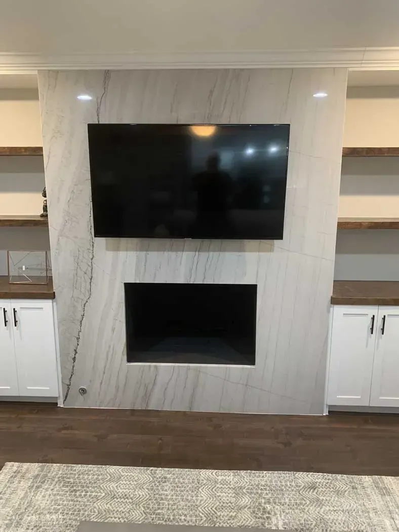 A modern fireplace with a large black TV above the recessed firebox, flanked by white cabinets and shelves.