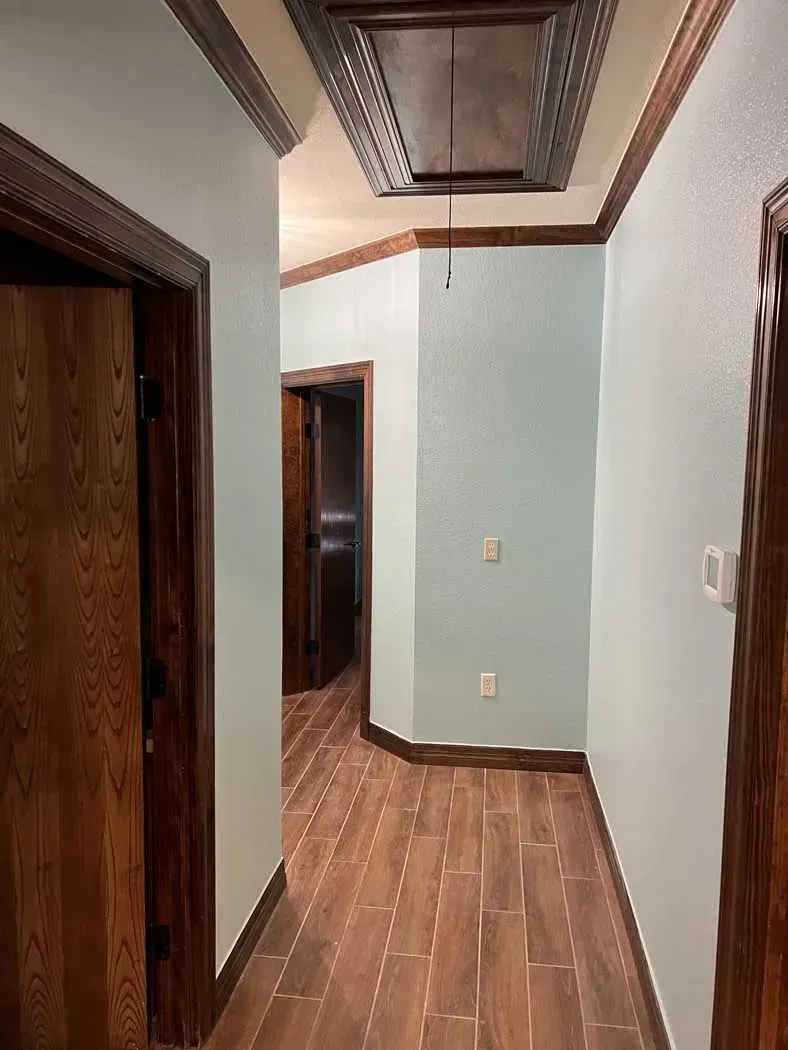 Hallway with light blue walls, wood trim, and a patterned ceiling panel.