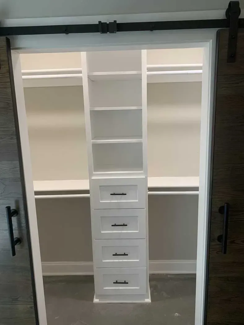 White closet organization with sliding barn doors. Center tower has shelves and drawers.