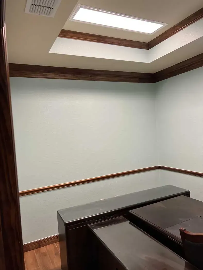 Empty office with light green walls, brown trim, and a recessed ceiling with a fluorescent light.
