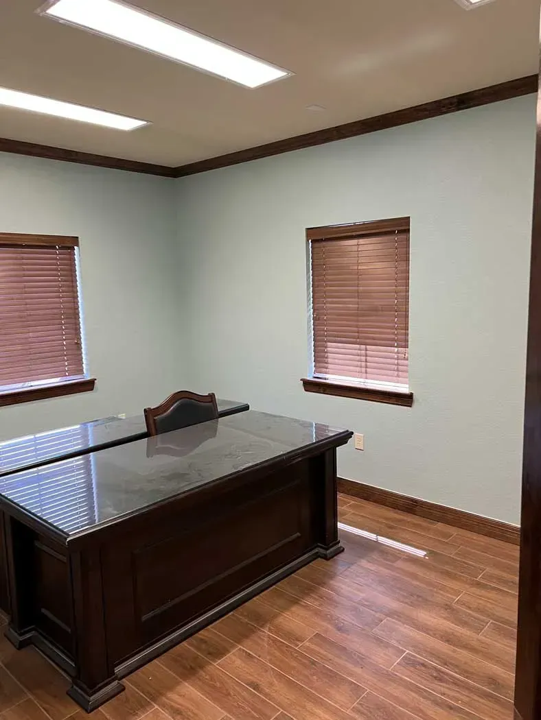 Empty office with a large dark wood desk, two windows with blinds, and wood trim.