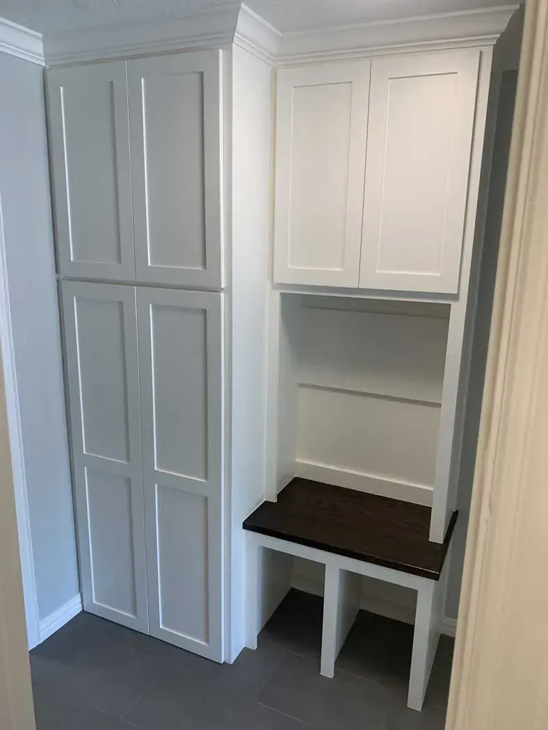 Built-in white cabinets and shelves with a bench in a hallway.