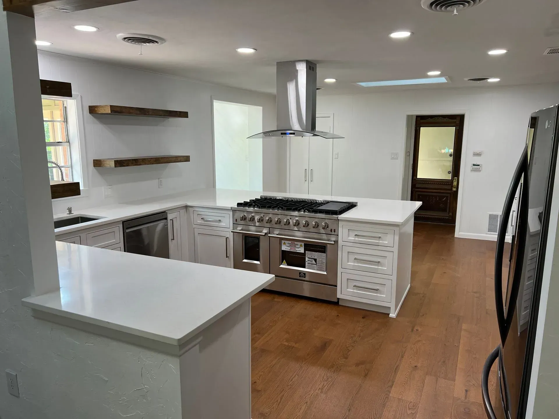 Modern kitchen with island, stainless steel range, white cabinets, wooden floors.