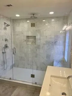 Modern bathroom with glass shower enclosure, marble tile, and white vanity.