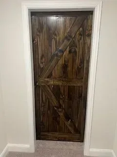 Dark wood barn door with diagonal brace, set in white doorframe.