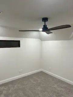 A room with gray carpet, white walls, and a black ceiling fan.
