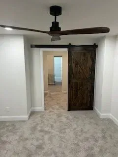 A dark wooden barn door slides on a black track. Brown ceiling fan and gray carpet.