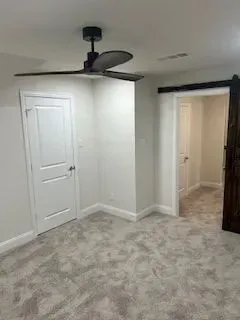 A room with white walls, carpet, and a ceiling fan; a white door and a sliding barn door are visible.