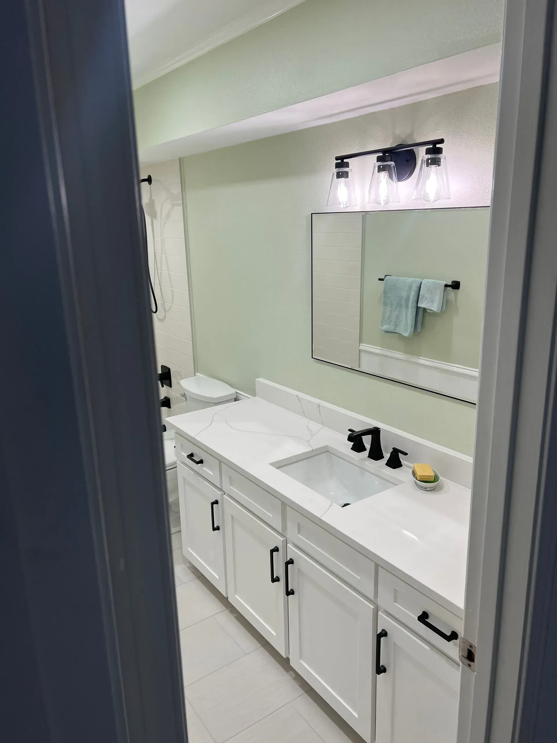 Bathroom with white cabinets, marble countertop, black fixtures, and a large mirror.