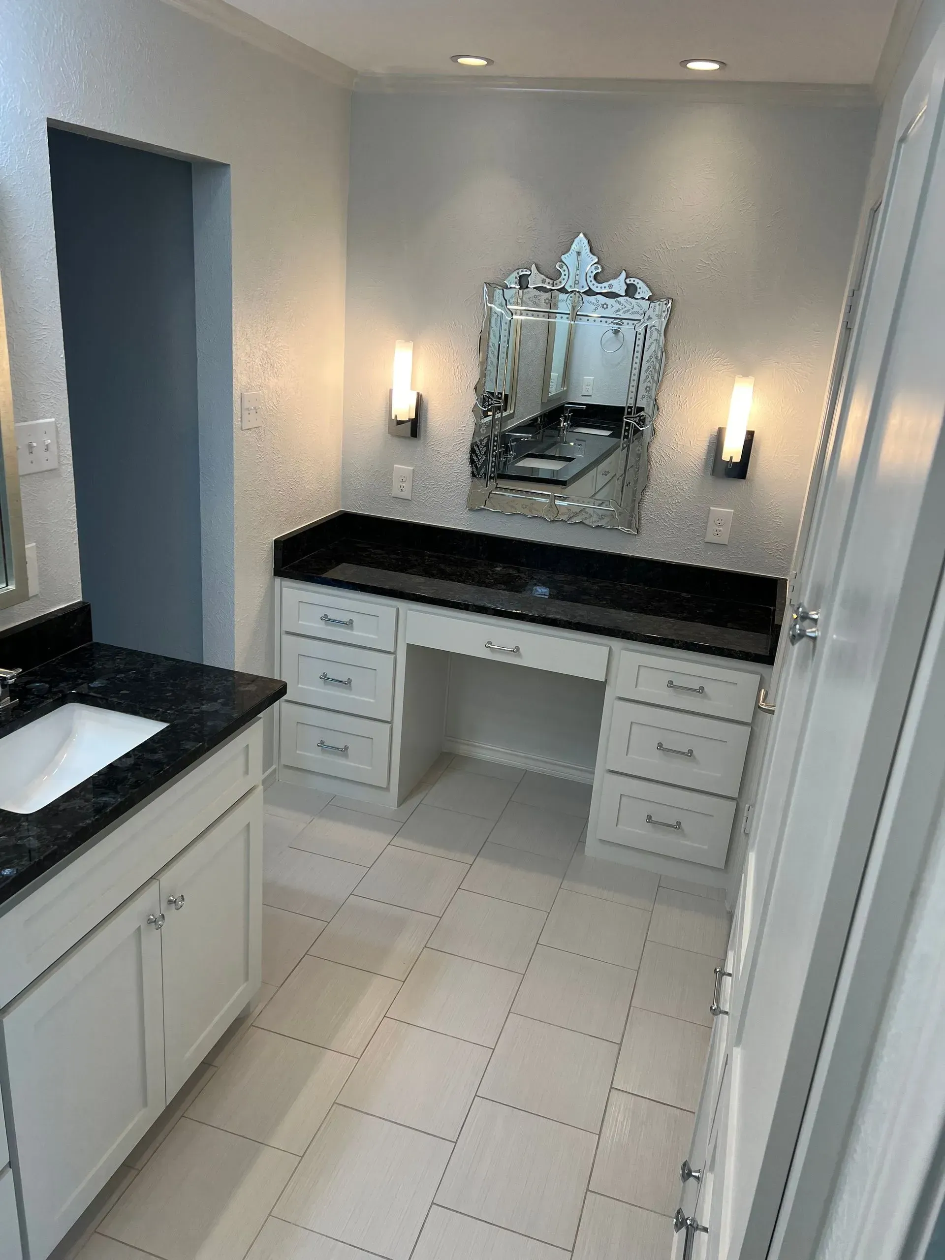 Bathroom with vanity, black countertop, white cabinets, decorative mirror, and sconce lighting.