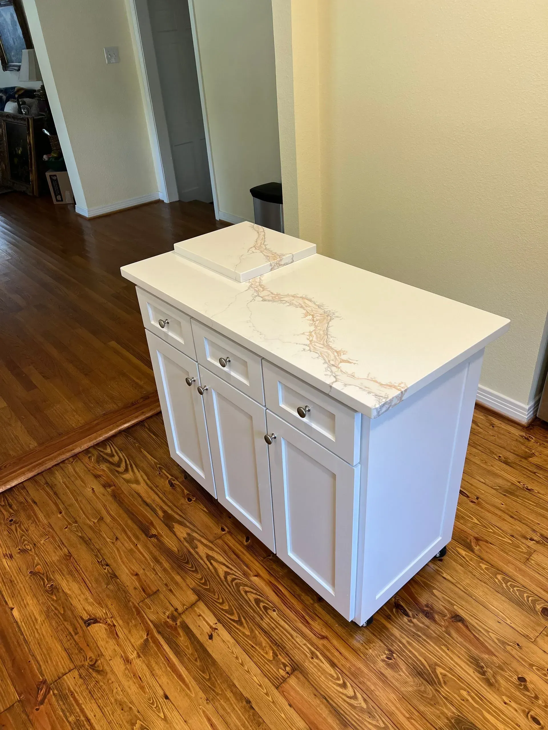 White kitchen island with countertop, cabinets, and a cutting board on hardwood floor.