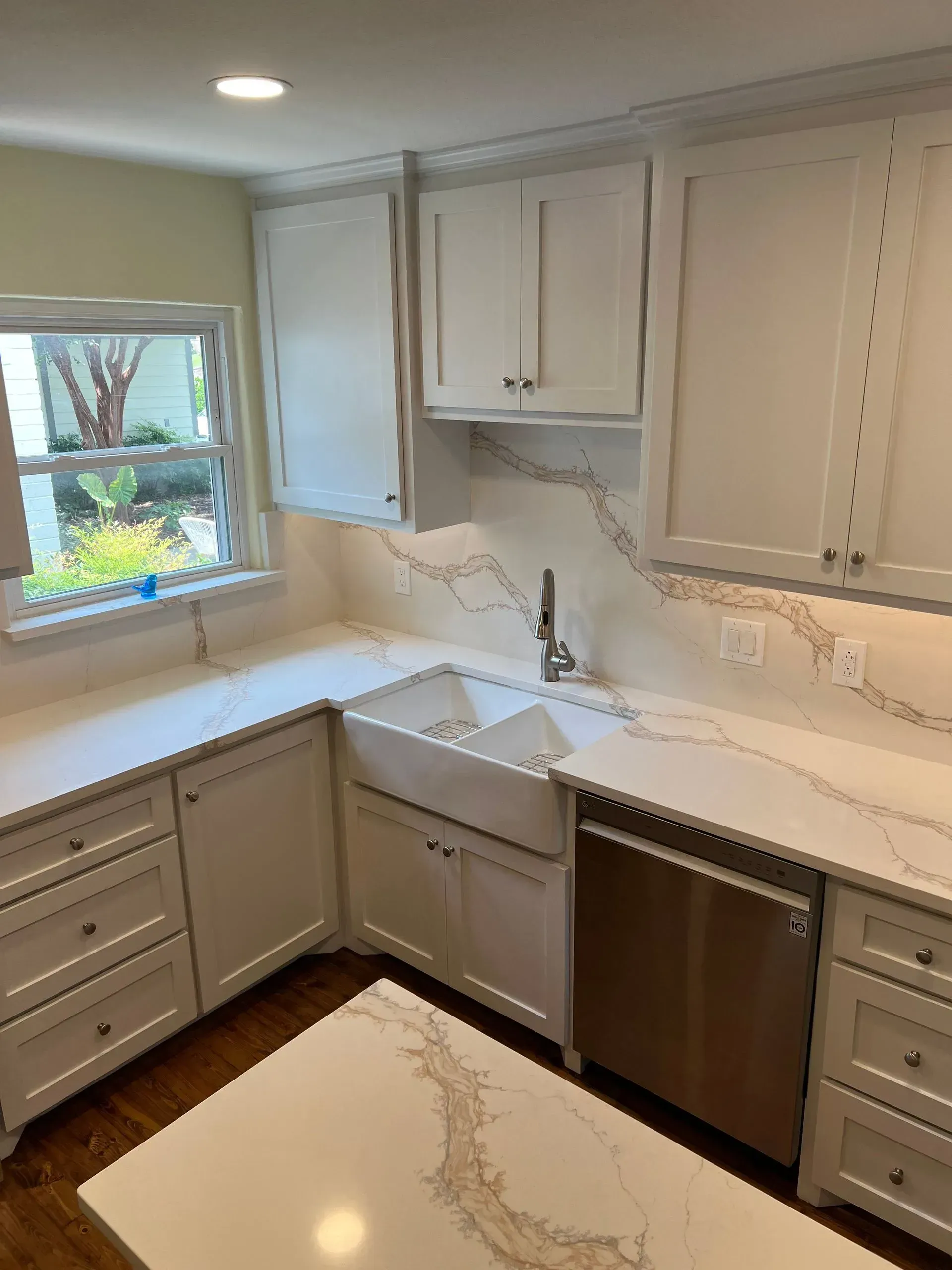 White kitchen with quartz countertops, cabinets, and a farmhouse sink. Stainless steel dishwasher.