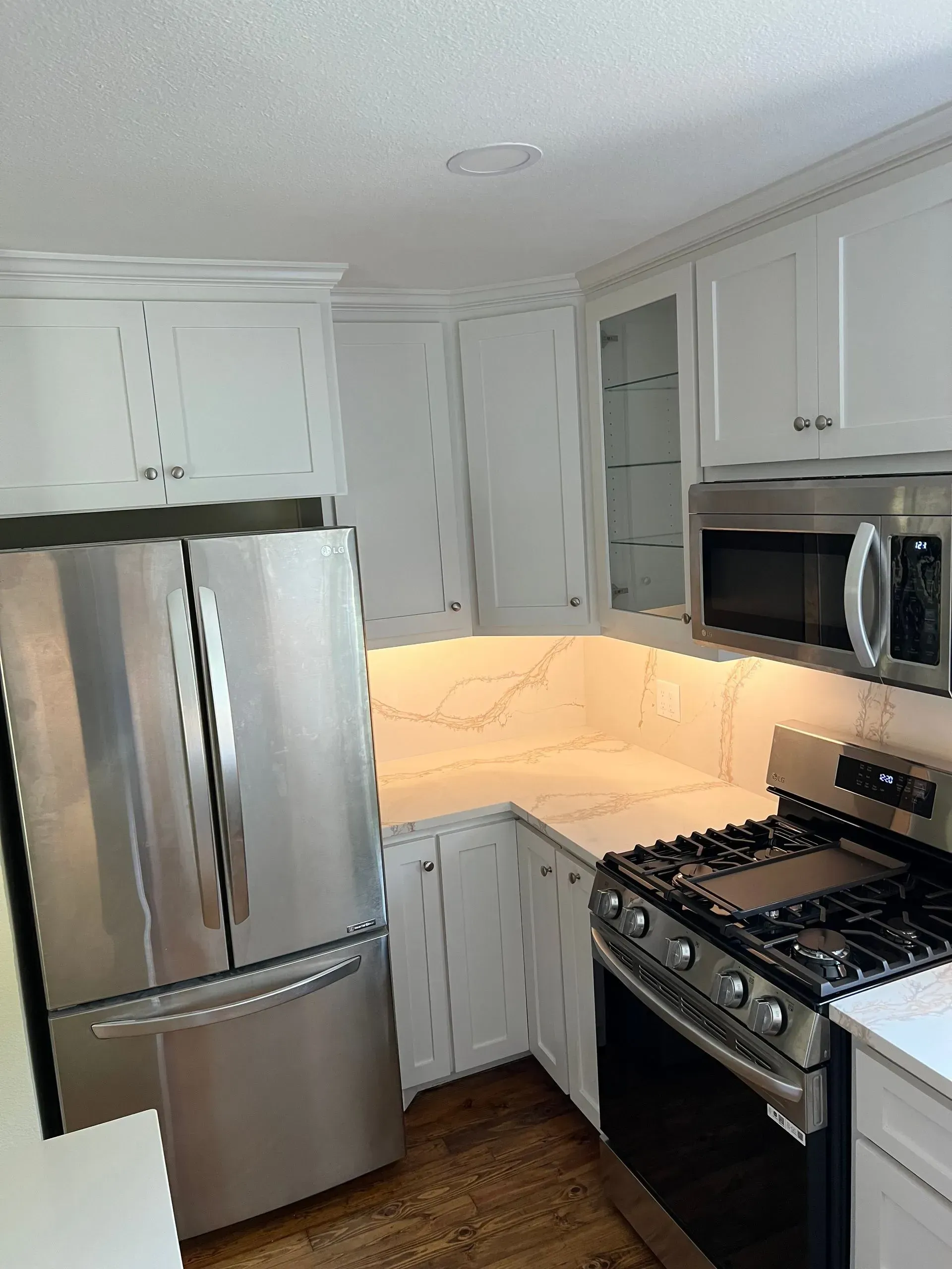 White kitchen with stainless steel appliances: refrigerator, microwave, and stove.