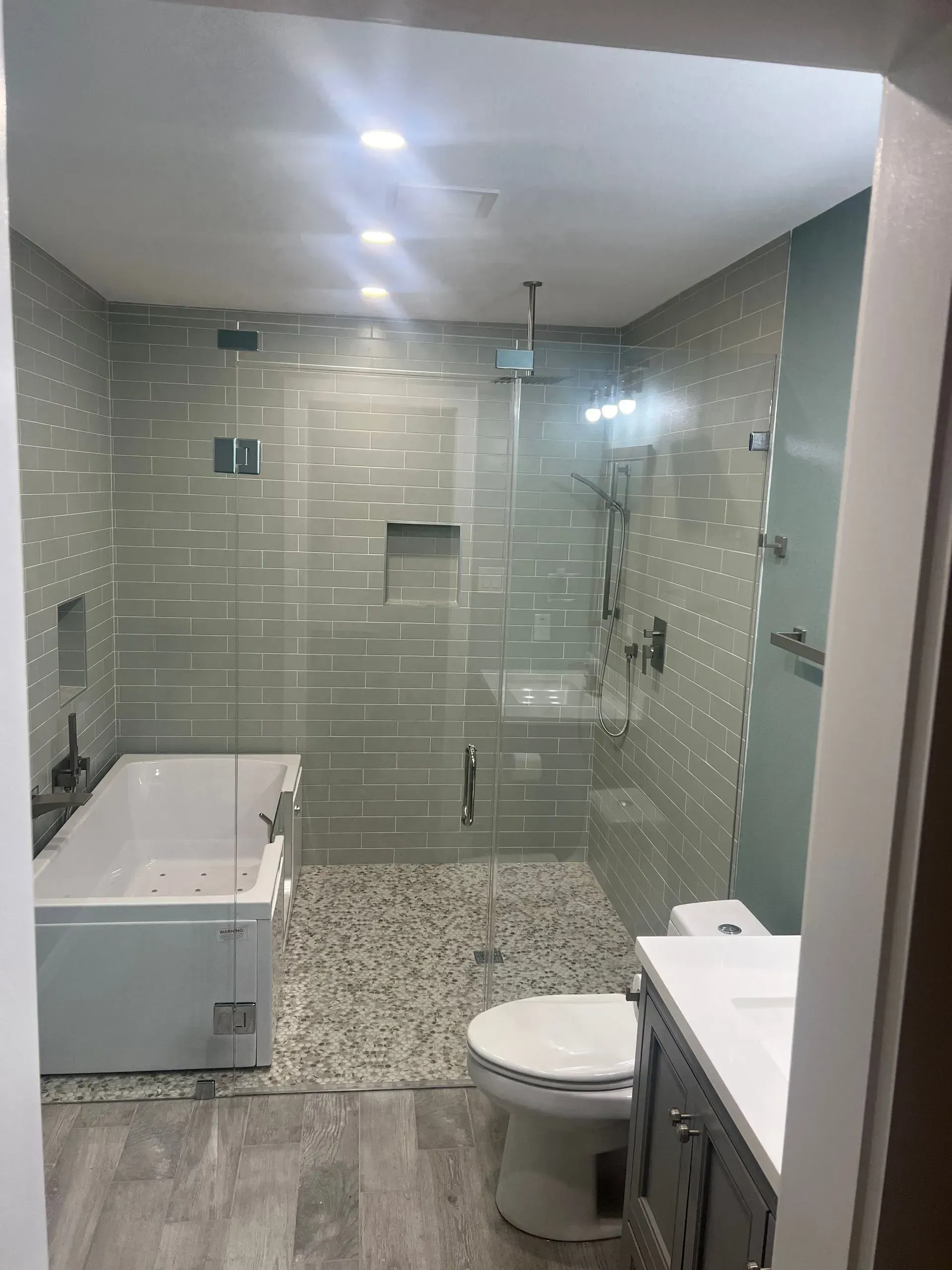 Modern bathroom with a glass-enclosed shower, bathtub, and toilet. Light green tile, gray and white accents.