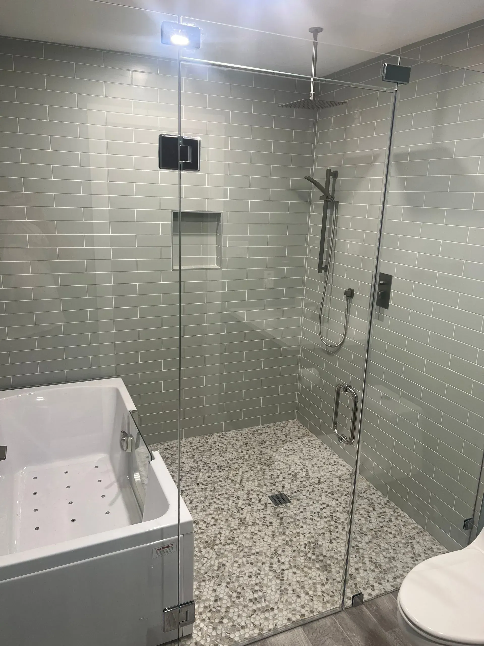 Modern bathroom with a glass shower enclosure, mosaic floor, and white tub.