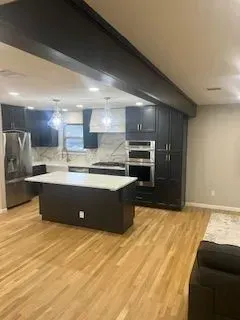 Modern kitchen with dark cabinetry, white countertops, stainless steel appliances, and wood flooring.