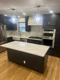 Modern kitchen with dark cabinets, white countertops, island, and two pendant lights.