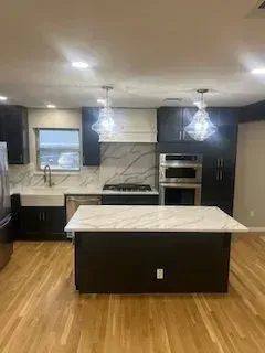 Modern kitchen with dark cabinetry, marble countertops, stainless steel appliances, and wooden flooring.