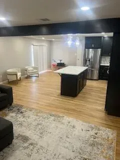 Open-concept kitchen and living area with island, dark cabinets, stainless steel appliances, and wood flooring.