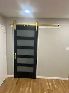 Black sliding barn door with frosted glass panels and gold hardware on a light wood wall.