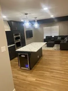 Modern kitchen and living room with dark cabinetry, marble island, hardwood floors, and dark sectional sofa.