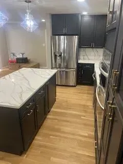 Modern kitchen with dark cabinets, stainless steel appliances, and a marble island countertop.