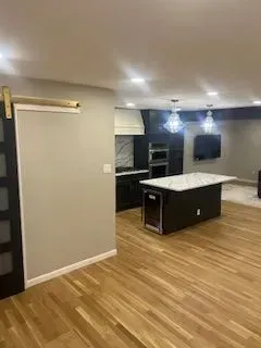Modern kitchen with dark cabinetry, white countertops, and hardwood floors.