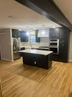 Newly renovated kitchen with dark cabinets, a white island, stainless steel appliances, and wooden floors.