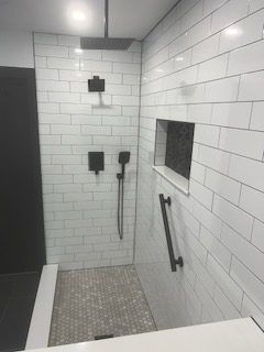 Modern tiled shower with a black showerhead, fixtures, and grab bar.