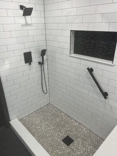 Modern shower with white subway tile walls, gray mosaic floor, black fixtures, and grab bar.