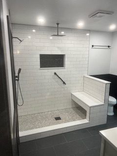 Accessible shower with white brick tile, bench, and grab bar.