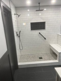 Bathroom with white subway tile shower, pebble floor, built-in seat, and dark fixtures.