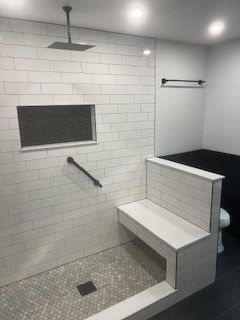 Bathroom with white tiled shower, bench, and handrail, gray mosaic floor.