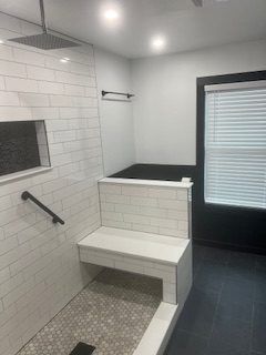 Bathroom with white tile, a shower bench, and a dark floor. A window with blinds is in the corner.