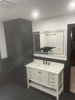 White vanity, large mirror, dark storage cabinet in a modern bathroom.