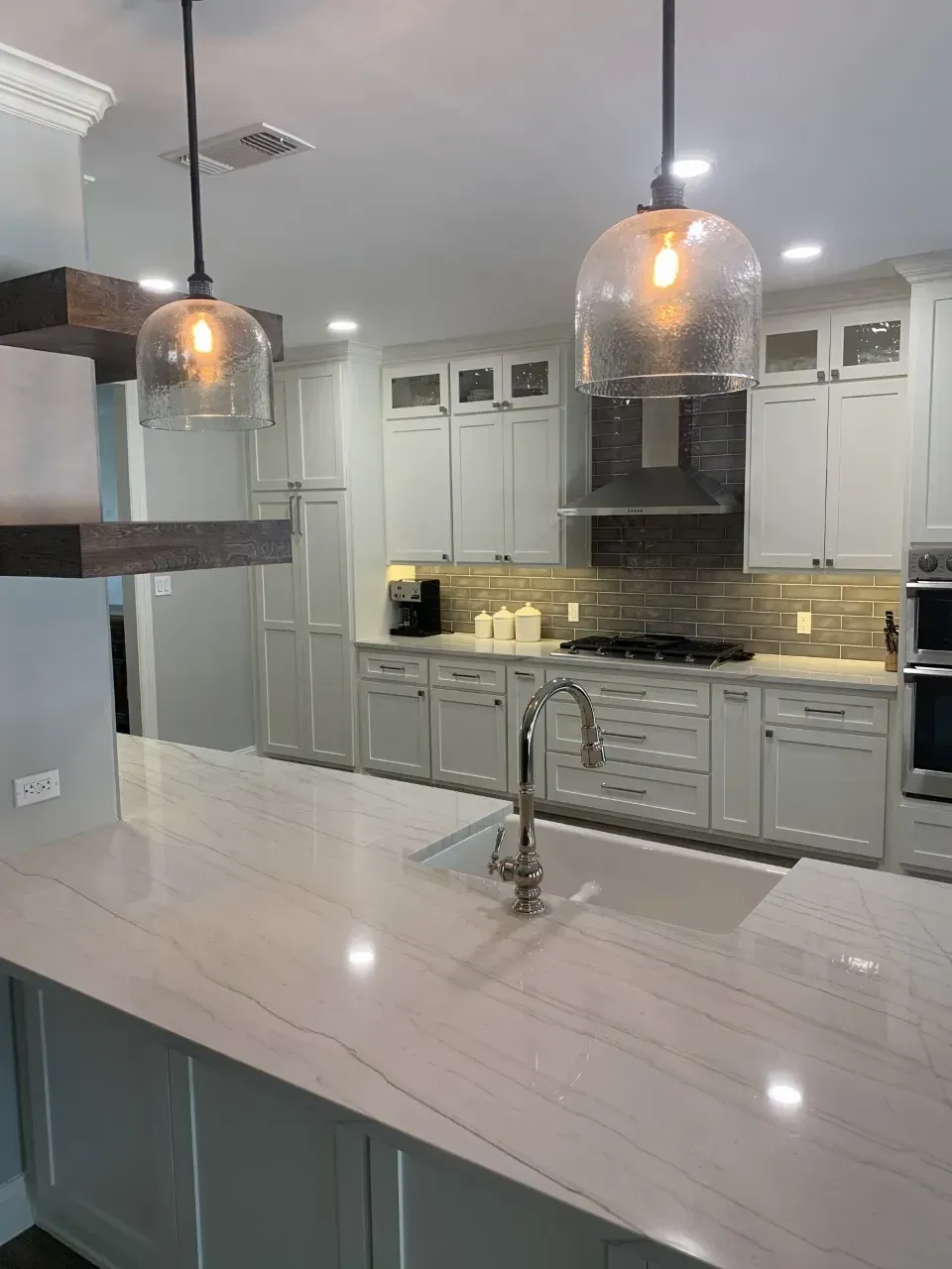 Modern kitchen with white cabinets, quartz countertops, and glass pendant lights.