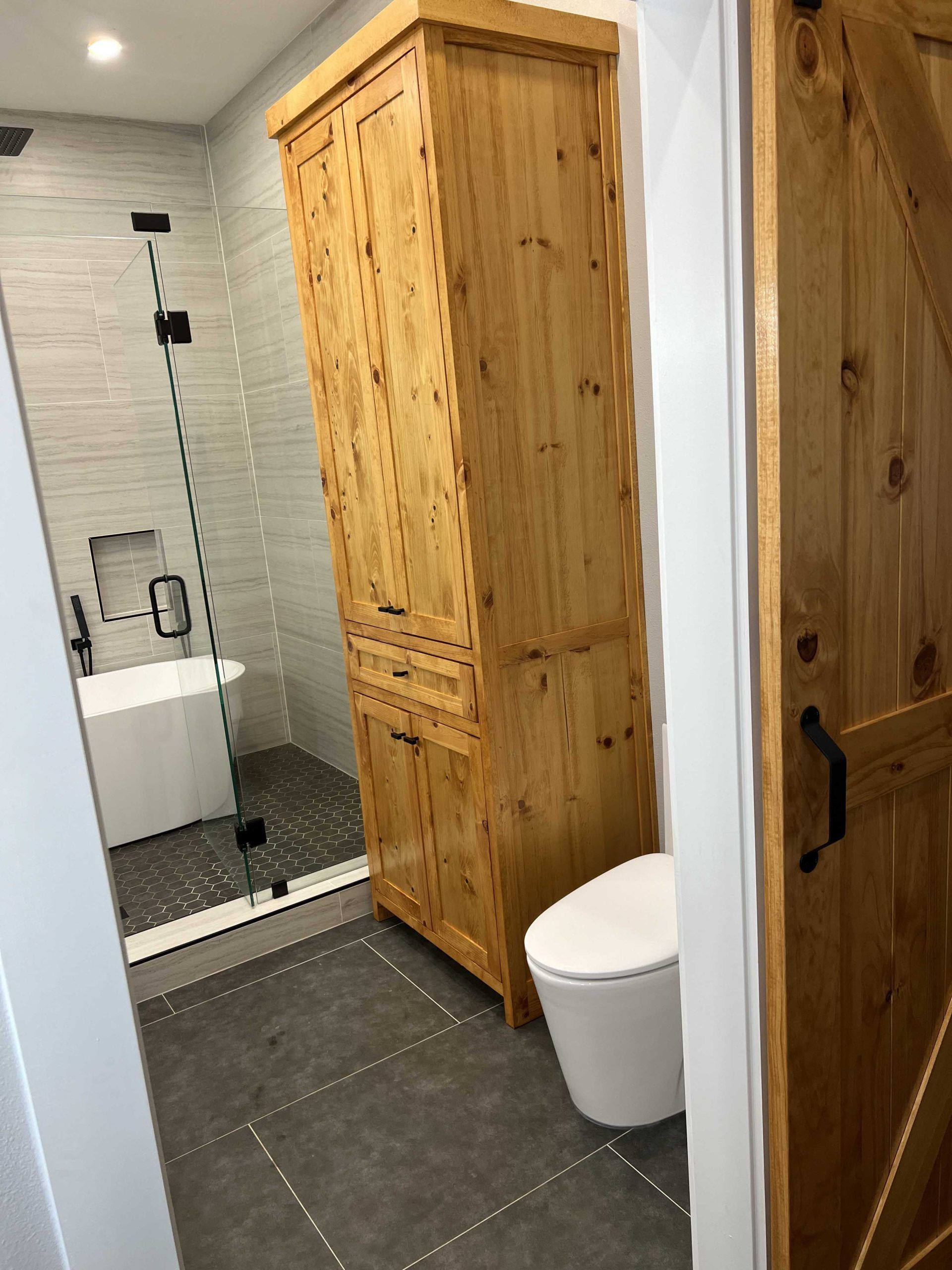 Bathroom with wooden cabinet, toilet, shower with glass door, and wooden door.